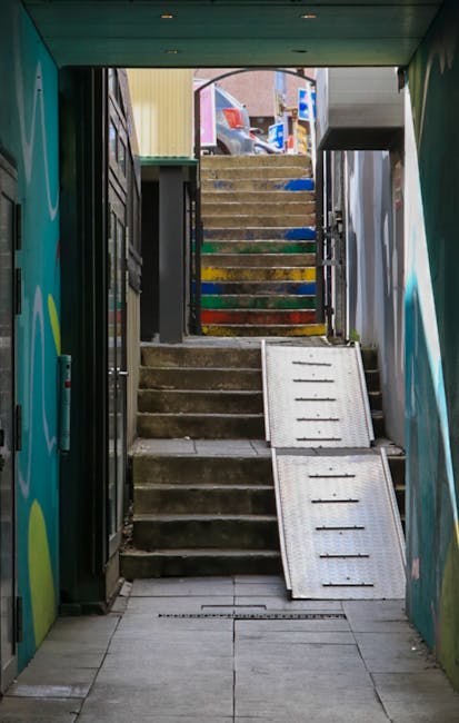 View from inside a stairwell leading to an outdoor staircase on narrow stairs with painted steps in various colors, including yellow, green, and blue. The entrance area features a concrete floor with