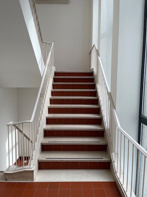 View from inside a stairwell leading to an outdoor staircase on narrow stairs with painted steps in various colors, including yellow, green, and blue. The entrance area features a concrete floor with
