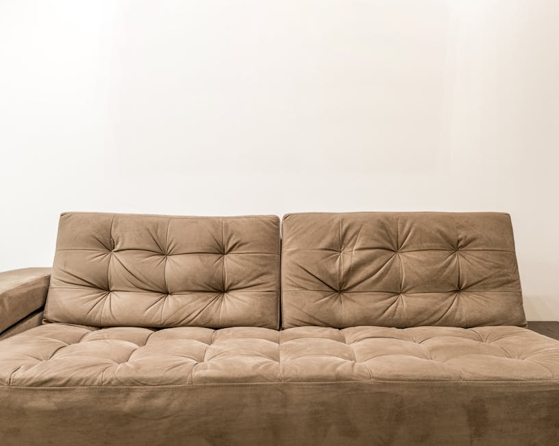 A modern living room featuring a large gray fabric sectional sofa adorned with light-colored cushions, situated on a neutral-toned carpet. In front of the sofa are two round, white coffee tables, one